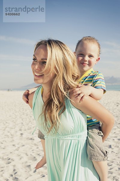 Mittlere erwachsene Mutter schenkt jungen Sohn Huckepack am Strand  Kapstadt  Westkap  Südafrika