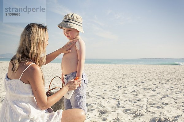 Mittlere erwachsene Mutter  die Sonnencreme auf den jungen Sohn am Strand aufträgt  Kapstadt  Westkap  Südafrika