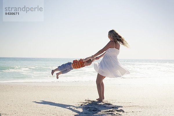 Mittlere erwachsene Mutter schwingt jungen Sohn von Hand am Strand  Kapstadt  Westkap  Südafrika