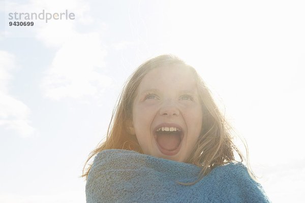 Porträt des lachenden Mädchens im Handtuch an der sonnenbeschienenen Küste