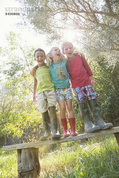 Drei Kinder stehen auf einem Gartensitz  die Arme umeinander.