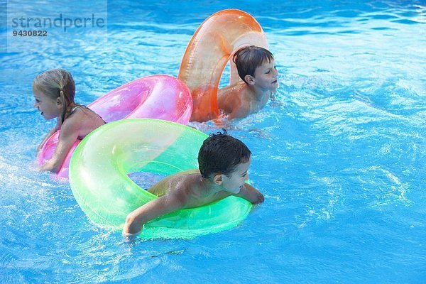 Drei Kinder spielen im Gartenschwimmbad mit aufblasbaren Ringen