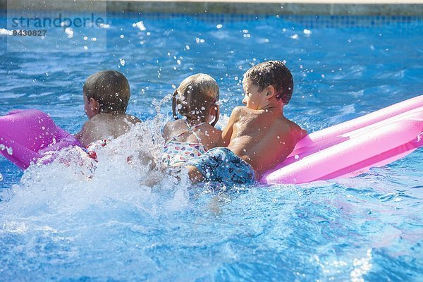 Rückansicht von drei Kindern  die auf einer aufblasbaren Matratze im Gartenschwimmbad spielen.
