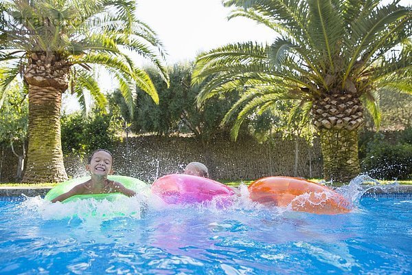 Drei Kinder planschen auf aufblasbaren Ringen im Gartenschwimmbad