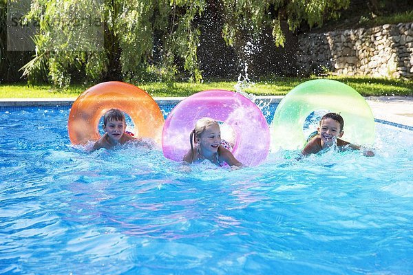Drei Kinder fahren auf auf aufblasbaren Ringen im Gartenschwimmbad