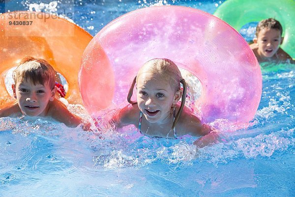 Drei Kinder schwimmen mit aufblasbaren Ringen im Gartenschwimmbad