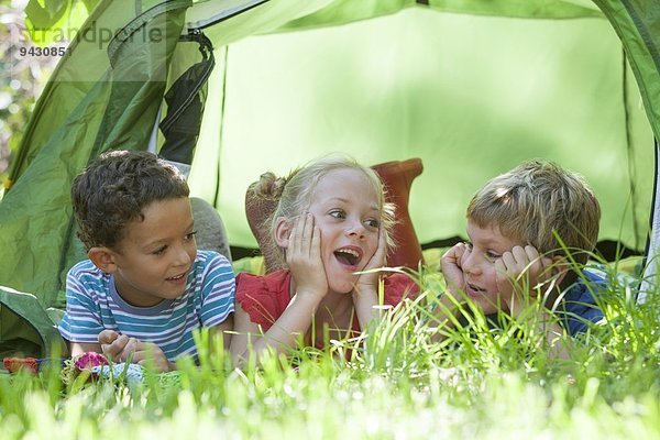 Drei Kinder liegend im Gartenzelt und plaudern