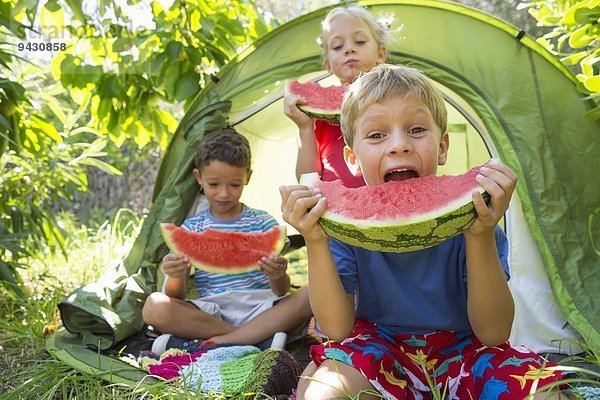 Drei Kinder essen große Wassermelonenscheiben im Gartenzelt