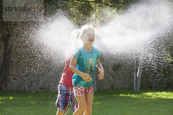 Junge jagt Mädchen im Garten mit Wasserberieselung