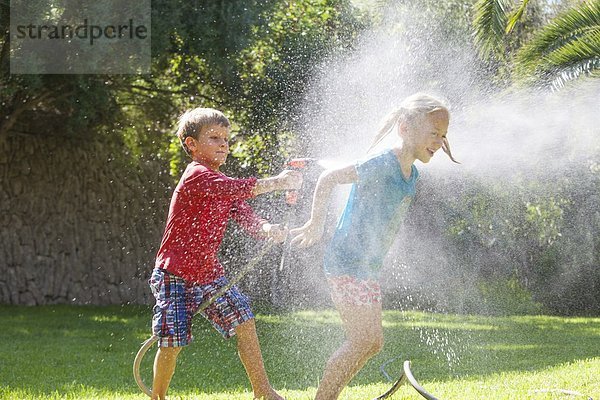 Junge spritzendes Mädchen im Garten mit Wasserberieselung