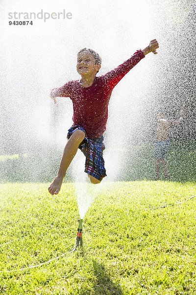 Junge springt über Wasserberieselung im Garten