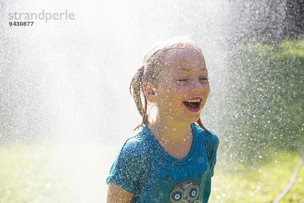 Mädchen wird im Garten von Wasserberieselung bespritzt