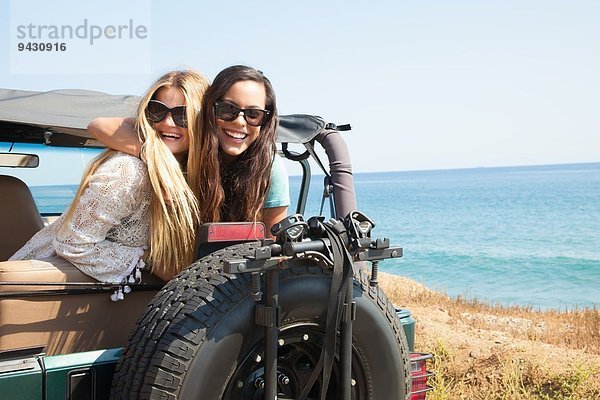 Porträt von zwei jungen Frauen  die sich aus dem Jeep an der Küste lehnen  Malibu  Kalifornien  USA