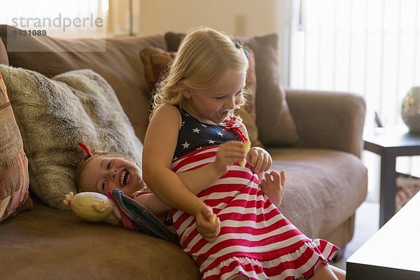 Mädchen auf älterer Schwester auf Sofa sitzend