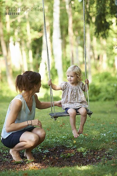 Mittlere erwachsene Mutter und Kleinkind-Tochter beim Spielen auf der Gartenschaukel