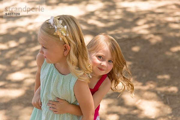 Junges Mädchen versteckt sich hinter Schwester im Park