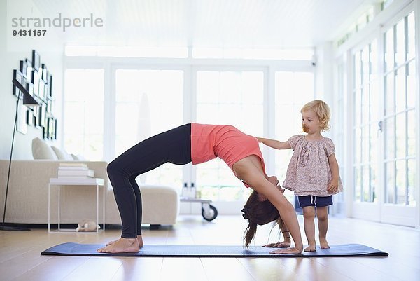 Mittlere erwachsene Mutter praktiziert Yoga mit neugieriger Kleinkind-Tochter