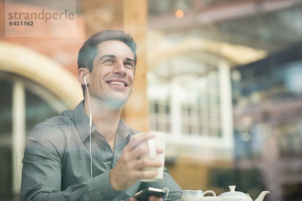 Junger Geschäftsmann hört Kopfhörer im Cafe Fenstersitz  London  UK