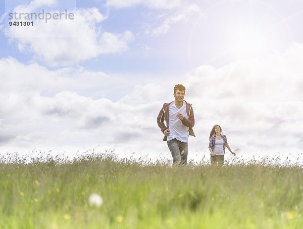 Junges Paar läuft bei strahlendem Sonnenschein durch die Wiese