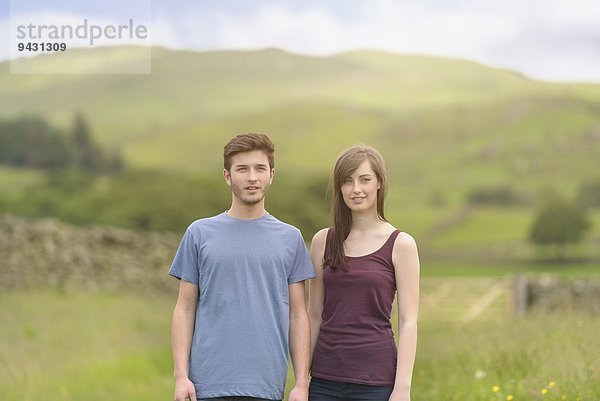 Junges Paar steht zusammen auf der Wiese und schaut weg über die ländliche Landschaft.