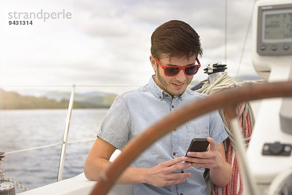 Junger Mann mit Handy auf der Yacht unter sonnigem Himmel