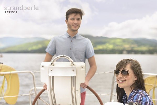 Junger Mann am Ruder der Yacht mit Freundin in Sonnenbrille