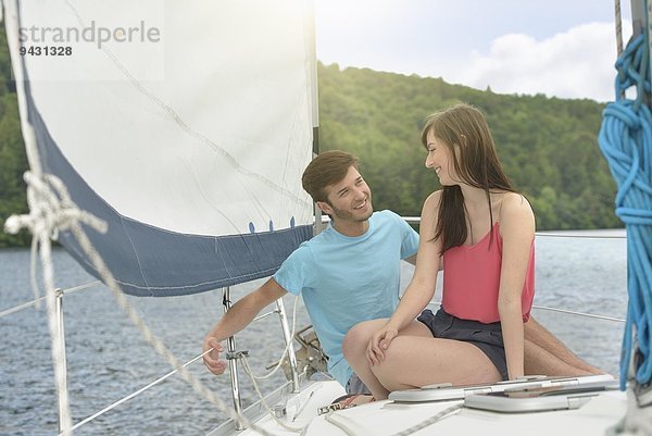 Junges Paar segelt auf einer sonnendurchfluteten Yacht über den See  lächelnd