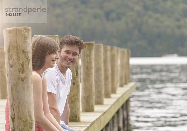 Junges Paar lacht gemeinsam am Steg über den See