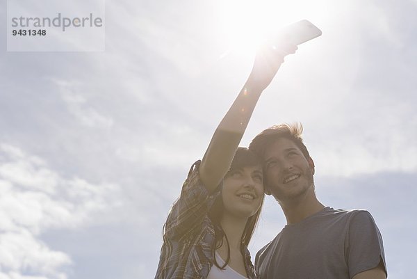 Junges Paar beim Selbstporträt auf dem Handy bei strahlendem Sonnenschein