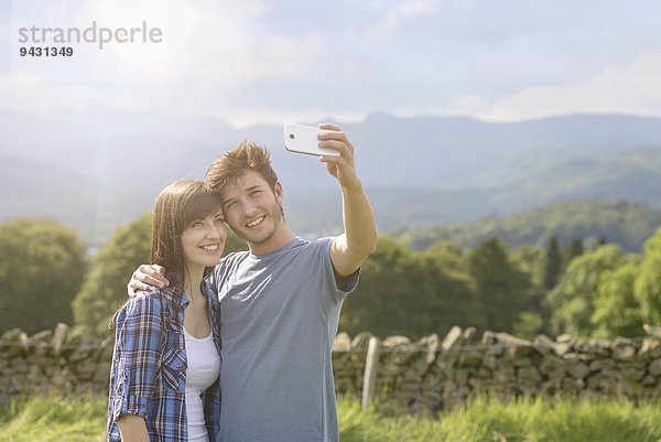 Junges Paar beim Selbstporträt auf dem Handy in der Natur unter sonnigem Himmel
