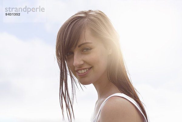 Porträt einer jungen Frau  die unter hellem Sonnenlicht lächelt.