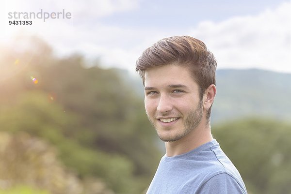 Porträt eines jungen Mannes  der unter hellem Sonnenlicht lächelt.