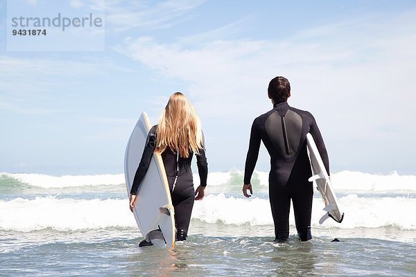 Junges Paar mit Surfbrettern auf dem Meer  Rückansicht