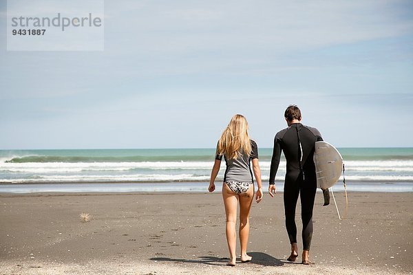 Junges Paar  das aufs Meer hinausgeht  junger Mann mit Surfbrett