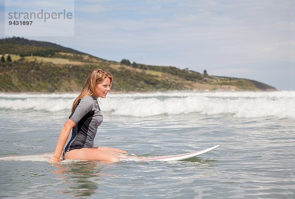 Portrait einer jungen Frau  die auf dem Surfbrett im Meer sitzt