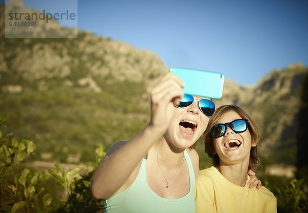 Schwester und Bruder machen Gesichter für Selfie auf Smartphone  Mallorca  Spanien