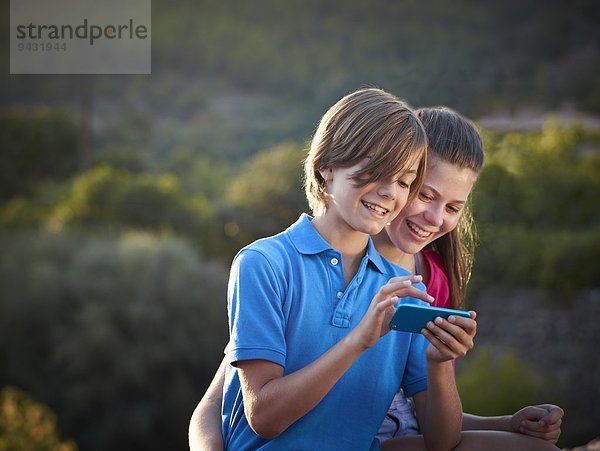 Bruder und jugendliche Schwester mit Touchscreen auf dem Smartphone  Mallorca  Spanien