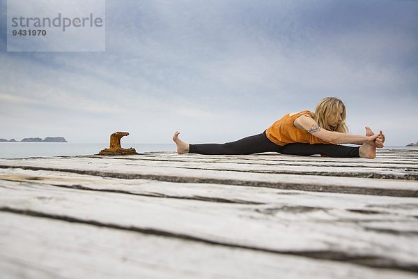 Mittlere erwachsene Frau  die Yoga auf einem hölzernen Pier praktiziert.