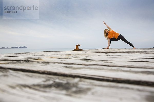 Mittlere erwachsene Frau praktiziert Yogastellung auf hölzernem Pier