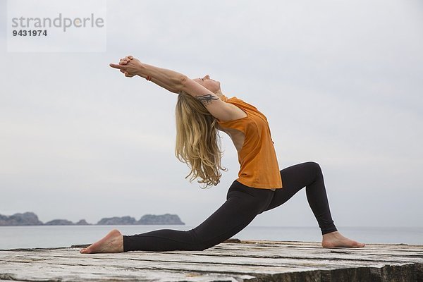 Mittlere erwachsene Frau  die sich nach hinten beugt und Yoga auf einem hölzernen Pier praktiziert.