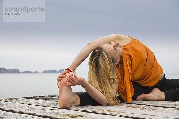 Mittlere erwachsene Frau  die Zehen berührt und Yoga auf einem hölzernen Pier praktiziert.