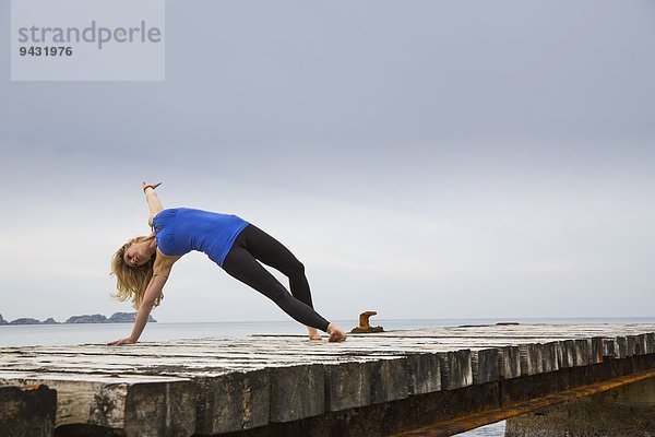 Mittlere erwachsene Frau  die Yoga übt  bewegt sich auf einem hölzernen Pier.