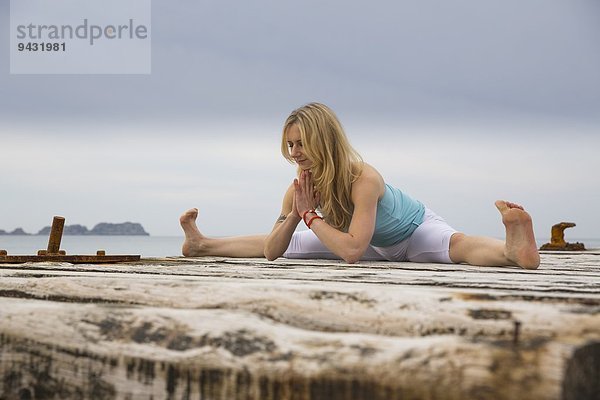 Mittlere erwachsene Frau mit gemeinsamen Händen  die Yoga auf einem hölzernen Pier praktiziert.