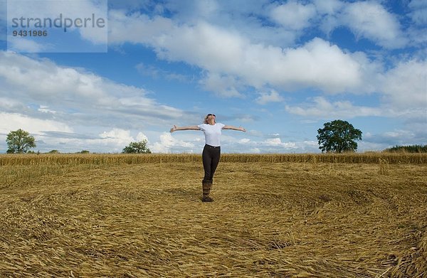 Reife Bäuerin feiert mit offenen Armen im geernteten Weizenfeld