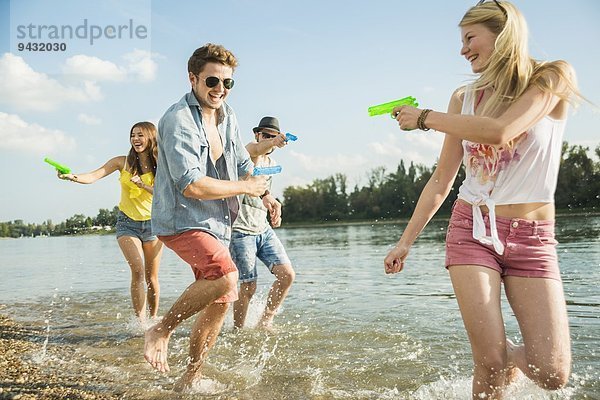 Freunde spielen mit Wasserpistolen im See