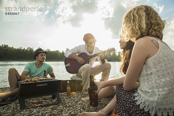 Junger Mann am See mit Freunden beim Gitarrespielen