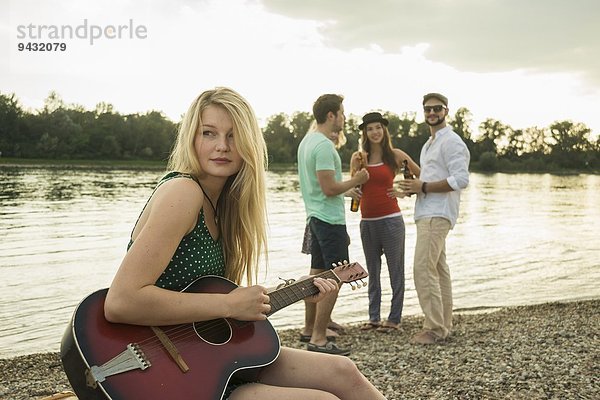 Junge Frau spielt Gitarre am See