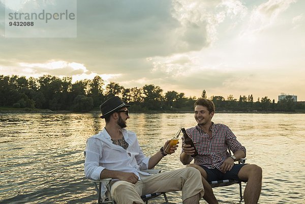 Junge Männer toasten mit Bierflaschen am See