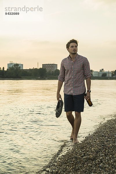 Junger Mann geht mit Schuhen am See entlang