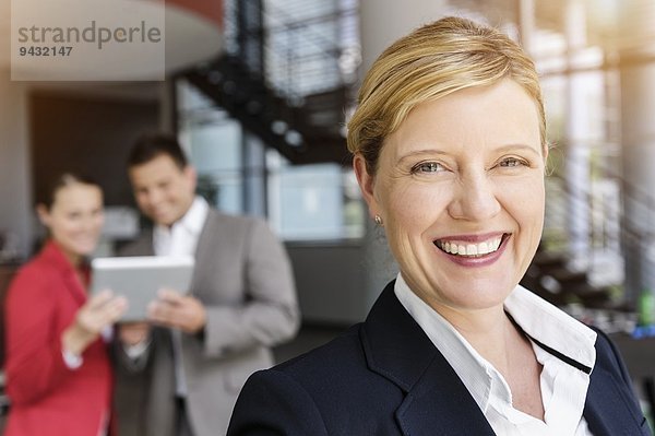 Lächelnde Geschäftsfrau  Kollegen im Hintergrund mit digitalem Tablett
